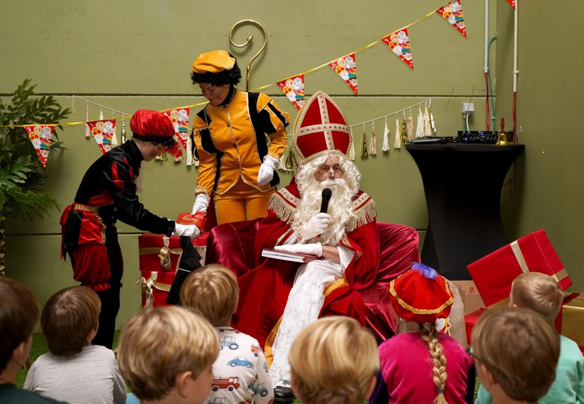 Sinterklaasviering met kinderen, waarbij Sinterklaas en zijn pieten cadeautjes uitdelen en met het publiek praten.